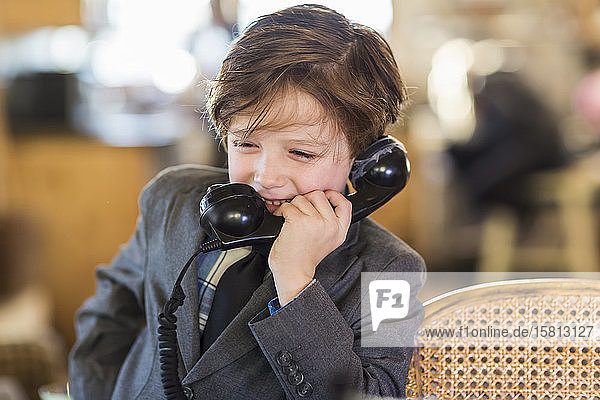 A six year old boy in a suit talking on a old vintage phone at home