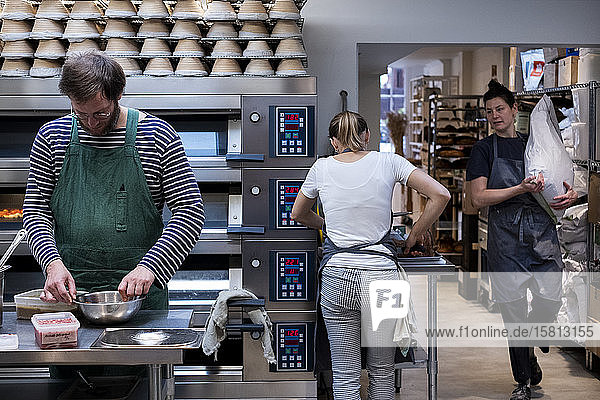 Zwei Frauen und ein Mann mit Schürzen  die in einer handwerklichen Bäckerei arbeiten.