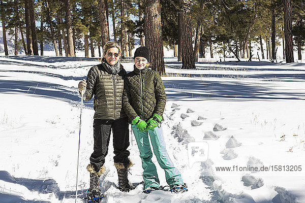 An adult woman and teenage girl in snow shoes in woodland holding ski poles