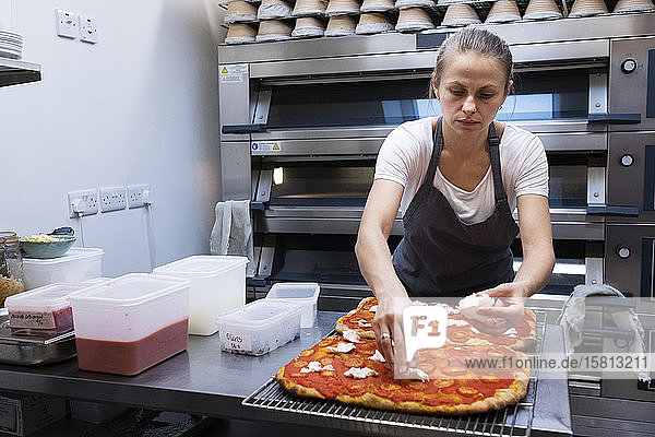 Frau mit Schürze steht in einer handwerklichen Bäckerei und bereitet Pizza zu.