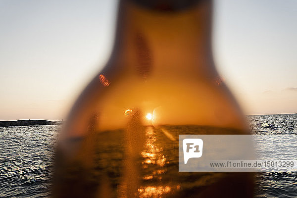 Sonnenuntergang über dem Meer durch braunes Glas Bierflasche