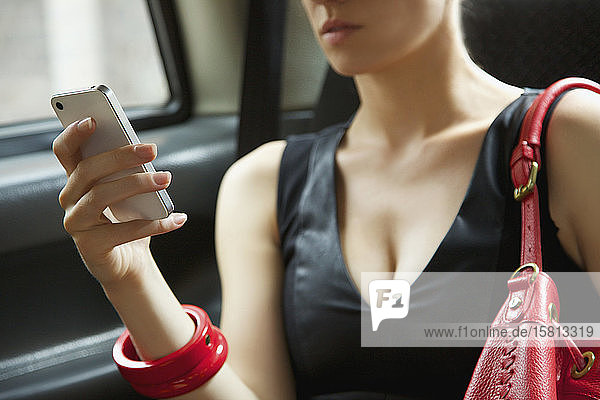 Close up stylish young woman using smart phone in back seat of taxi
