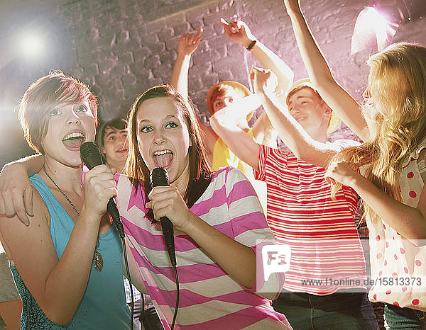 Happy teenage friends singing karaoke at party