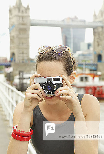 Porträt einer jungen Frau mit Retro-Kamera vor der Tower Bridge  London