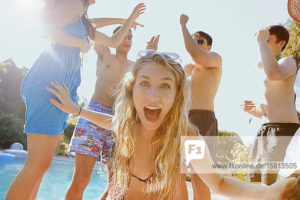 Portrait exuberant teenage girl dancing with friends at sunny summer poolside
