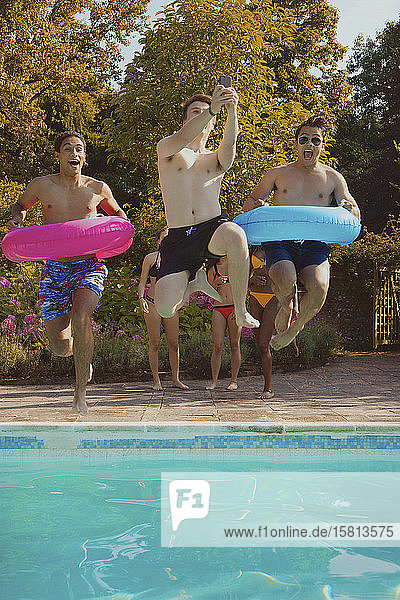Verspielte Teenager-Freunde mit aufblasbaren Ringen  die ins Schwimmbad springen