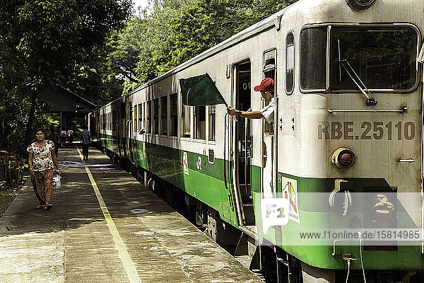 Ein Personenzug im Bahnhof Lanmadaw mit einem Zugführer  der eine grüne Fahne schwenkt  und einem Fahrgast auf dem Bahnsteig  Yangon (Rangun)  Myanmar (Burma)  Asien