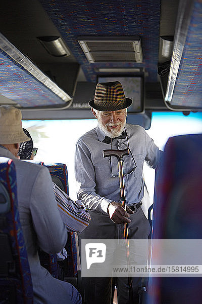 Aktiver älterer Mann mit Hut und Gehstock beim Einsteigen in einen Reisebus