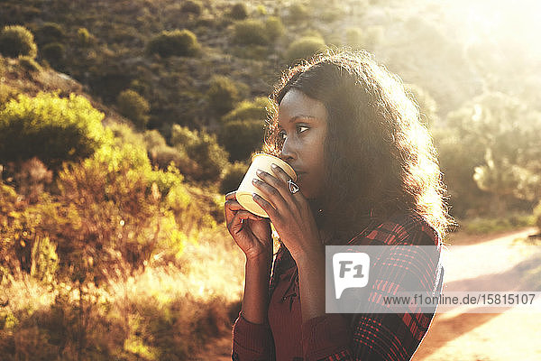 Junge Frau trinkt Kaffee im sonnigen Wald