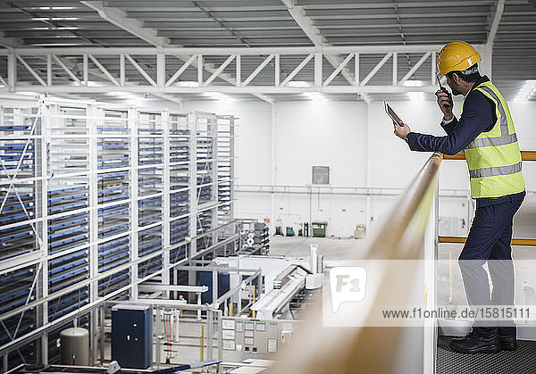 Male supervisor with digital tablet talking  using walkie-talkie on platform in factory