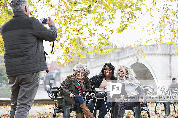 Senior man photographing active senior women friends at autumn park cafe