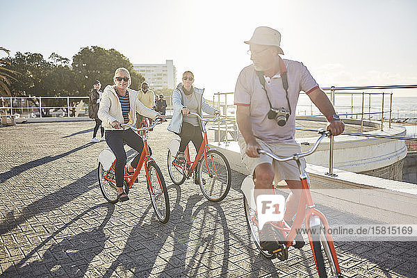 Active senior tourist friends bike riding on sunny boardwalk