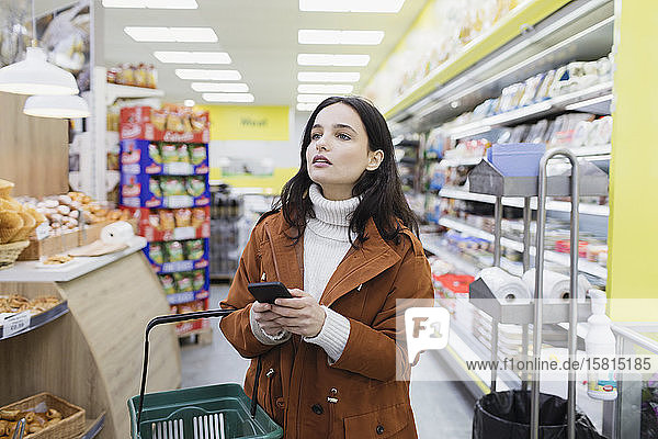 Frau mit Smartphone beim Einkaufen im Supermarkt
