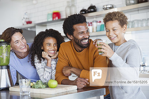 Multiethnische Familie macht und trinkt gesunden grünen Smoothie in der Küche