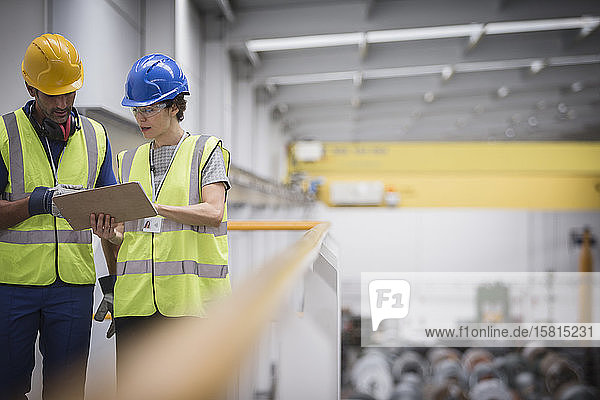 Aufsichtspersonen mit Klemmbrett im Gespräch auf einer Plattform in einer Fabrik