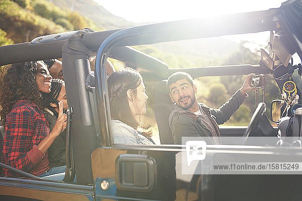 Mann mit Digitalkamera macht Selfie im Jeep mit Freunden