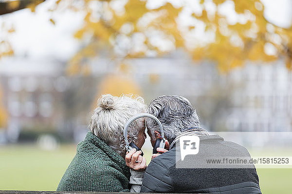 Älteres Paar mit Kopfhörern  das im Herbst im Park Musik hört