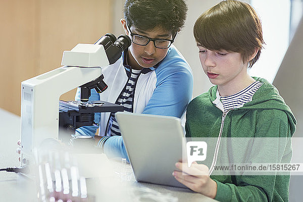 Fokussierter Junge  der ein digitales Tablet am Mikroskop im Laborunterricht benutzt