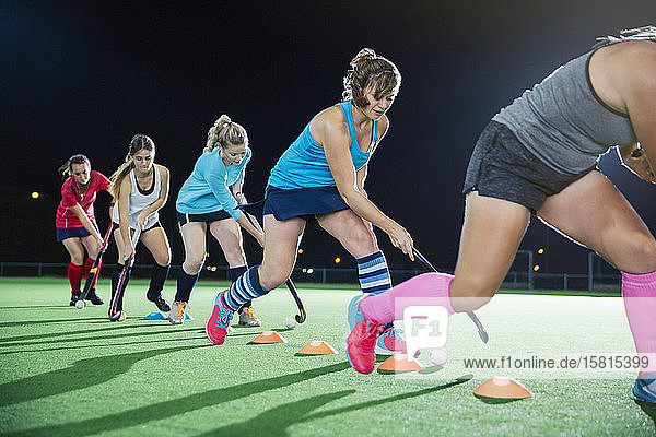 Young female field hockey players practicing sports drill on field at night