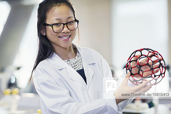 Porträt einer lächelnden  selbstbewussten Studentin  die eine molekulare Struktur in einem Laboratorium hält