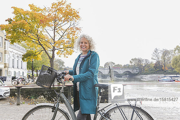 Porträt lächelnd ältere Frau Fahrradfahren entlang Herbst Fluss