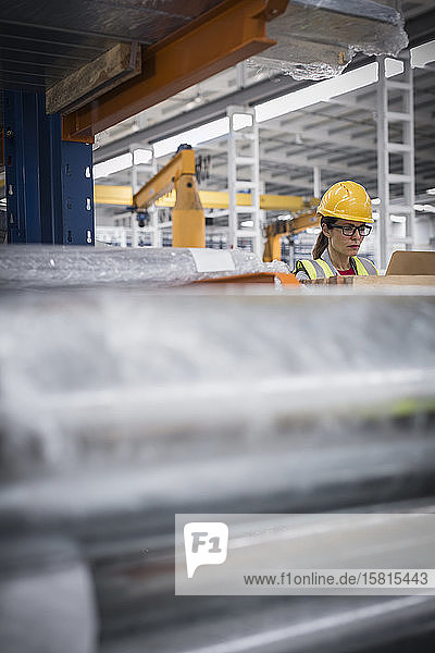 Focused female worker using laptop in steel factory