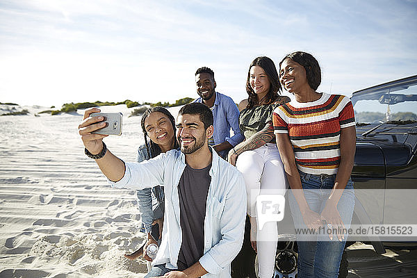 Young friends with camera phone taking selfie on beach