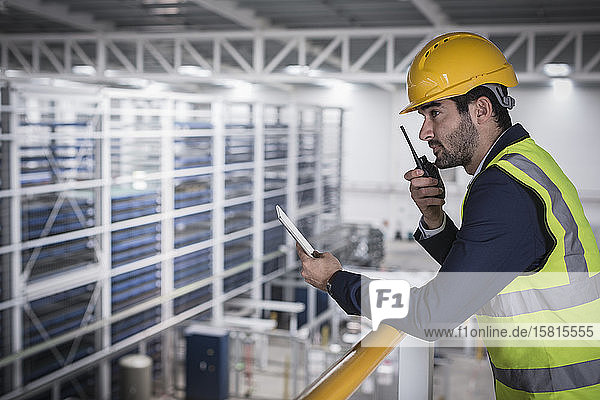 Männlicher Vorgesetzter mit digitalem Tablet im Gespräch  mit Walkie-Talkie n-Plattform in der Fabrik