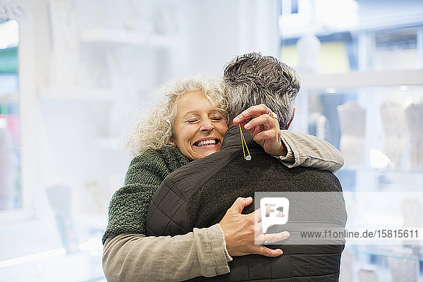 Lächelnde ältere Frau  die ihren Mann in einem Juweliergeschäft umarmt