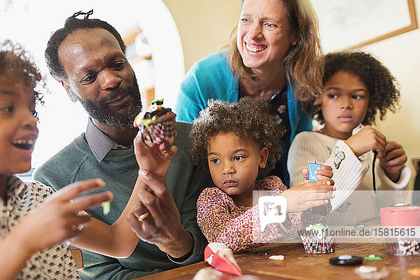 Happy multiethnic family decorating cupcakes at table