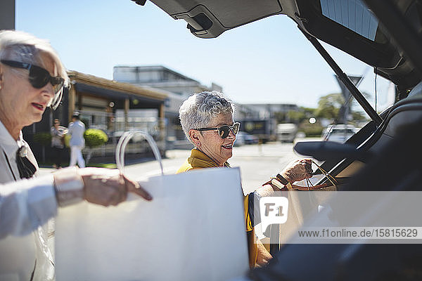 Senior women loading shopping bags into back of car in sunny parking lot