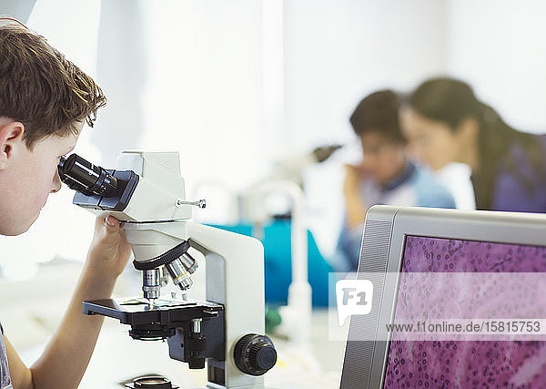 Junge Student  der ein Mikroskop benutzt und ein wissenschaftliches Experiment in einem Laboratorium durchführt