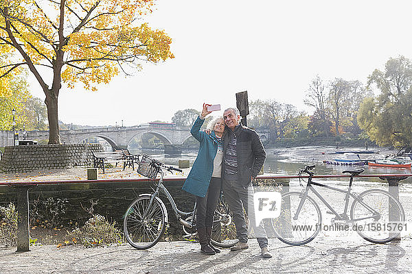Senior couple with bicycles taking selfie at autumn river