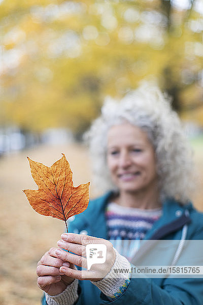 Ältere Frau hält orangefarbenes Herbstblatt im Park