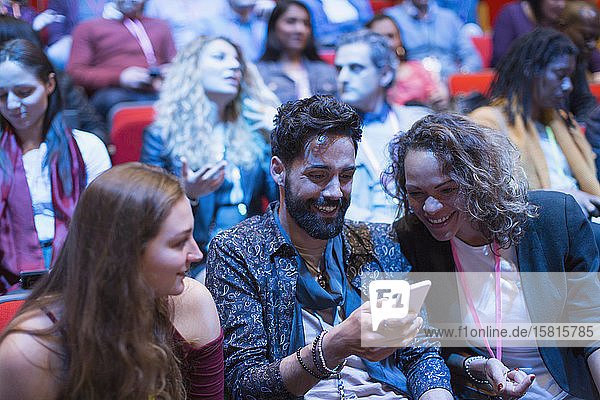 Lächelnde Geschäftsleute  die in einer Konferenz ein Smartphone benutzen