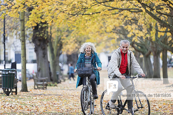 Älteres Paar fährt mit dem Fahrrad zwischen Bäumen und Blättern im Herbstpark