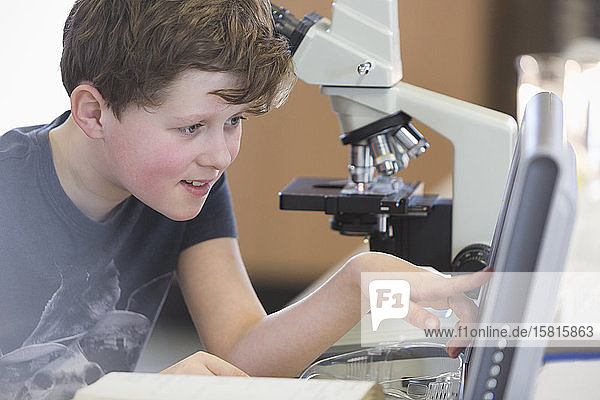 Junge Student  der ein wissenschaftliches Experiment am Mikroskop und Computer im Labor-Klassenzimmer durchführt