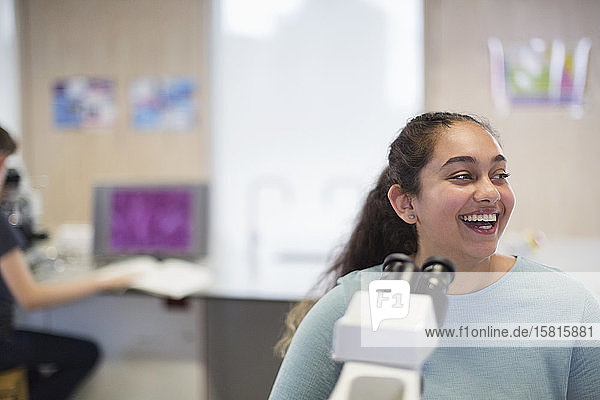 Laughing girl student at microscope in laboratory classroom