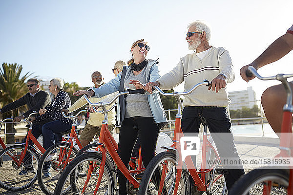 Aktive ältere Touristenfreunde beim Radfahren auf der sonnigen Strandpromenade