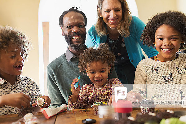 Porträt einer glücklichen multiethnischen Familie  die am Tisch Törtchen verziert
