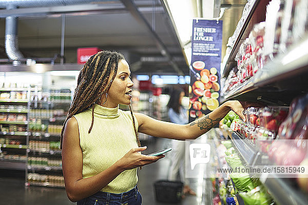 Frau mit Smartphone beim Lebensmitteleinkauf im Supermarkt