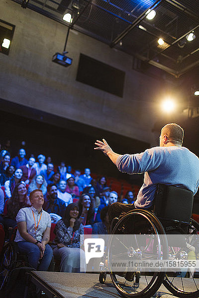 Publikum beobachtet männlichen Redner im Rollstuhl  der auf der Bühne spricht