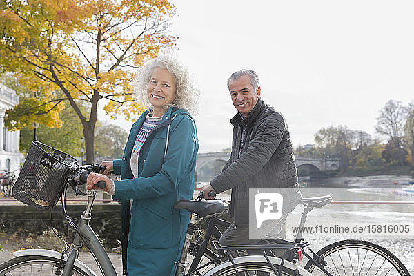 Portrait smiling senior couple bike riding along autumn river