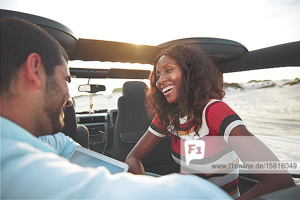 Lächelndes junges Paar auf dem Rücksitz eines Jeeps am Strand  das einen Roadtrip genießt