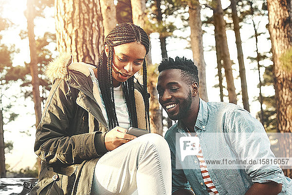 Junges Paar  das mit seinem Smartphone im Wald SMS schreibt