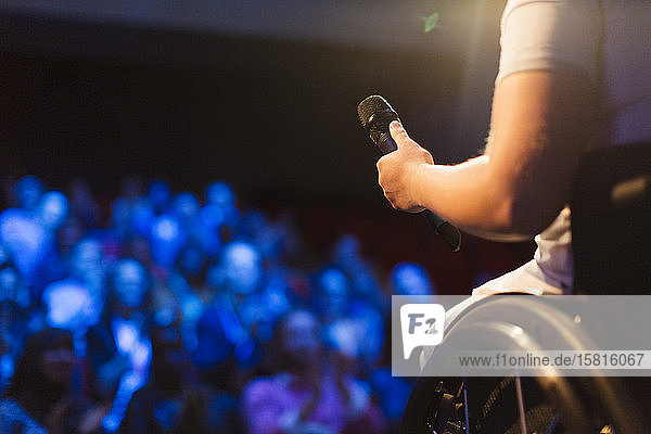 Female speaker in wheelchair holding microphone on stage