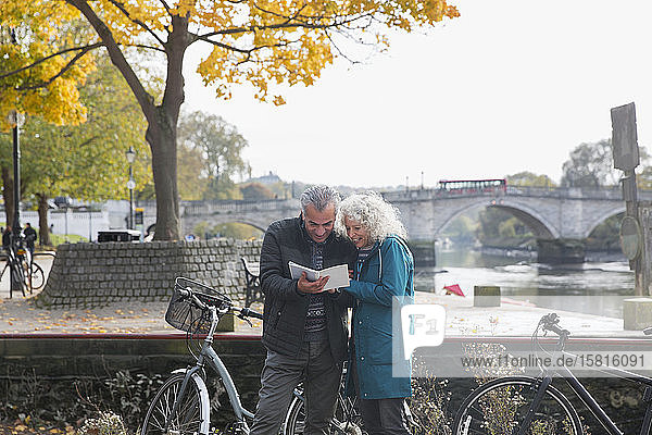 Älteres Ehepaar mit Fahrrädern unterwegs  Blick in einen Reiseführer entlang eines herbstlichen Flusses