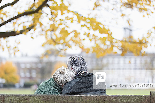 Zärtliches älteres Paar kuschelt auf einer Bank im Herbstpark