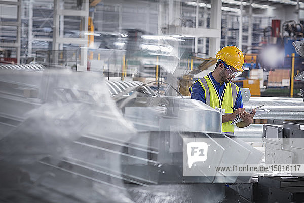 Fabrikarbeiter mit Klemmbrett bei der Kontrolle von Stahlteilen in einer Fabrik