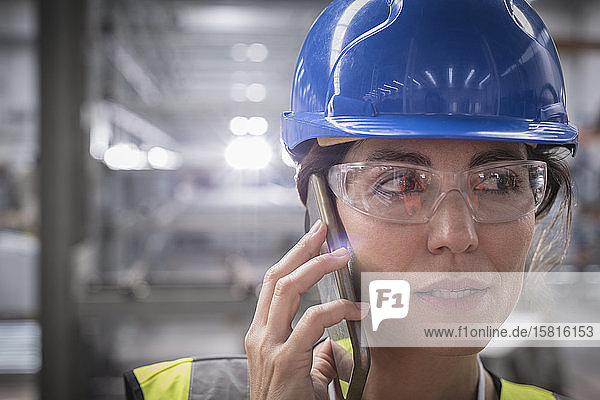 Nahaufnahme eines weiblichen Arbeiters  der in einer Fabrik mit einem Smartphone telefoniert